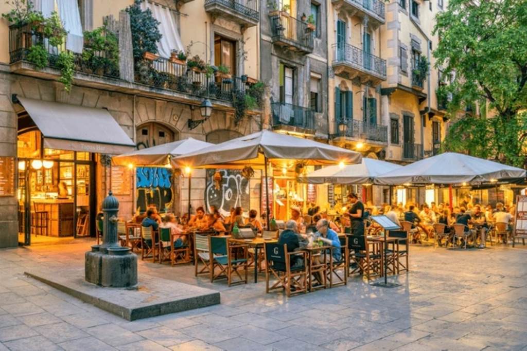 Vibrant street scene in El Born with tapas restaurants and historic buildings under a sunset sky